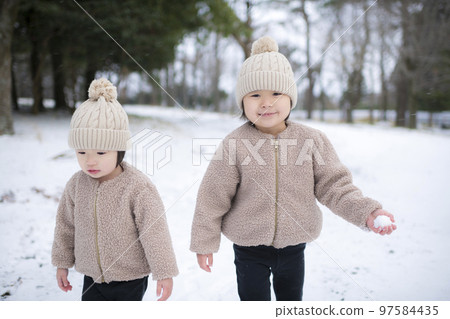 Girl sisters wearing knitted hats playing in the snow in winter Girl sisters wearing knitted hats playing in the snow in winter 97584435