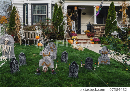 Many colorful Halloween decorations, skeletons, scarecrows at driveway and front lawn of house. Many colorful Halloween decorations, skeletons, scarecrows at driveway and front lawn of house. 97584482