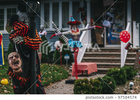Many colorful Halloween decorations, skeletons, scarecrows at driveway and front lawn of house. 97584574