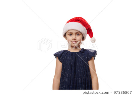 Isolated portrait on white background of a Caucasian 5-6 years old child, cute little girl in elegant navy dress and Santa hat, smiles looking confidently at camera. Christmas and New Year's concept Isolated portrait on white background of a Caucasian 5-6 years old child, cute little girl in elegant navy dress and Santa hat, smiles looking confidently at camera. Christmas and New Year's concept 97586867