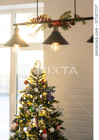 The black lampshade in the industrial loft style is decorated with spruce branches for Christmas and New Year on the background white brick wall. Close-up, minimalism The black lampshade in the industrial loft style is decorated with spruce branches for Christmas and New Year on the background white brick wall. Close-up, minimalism 97587337