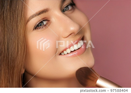 Beautiful young woman applying cosmetic powder product with make-up bamboo brush, beauty, makeup and skincare cosmetics model face portrait on pink background, closeup Beautiful young woman applying cosmetic powder product with make-up bamboo brush, beauty, makeup and skincare cosmetics model face portrait on pink background, closeup 97588404