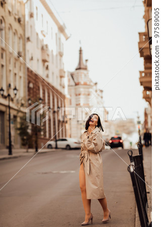 a beautiful brunette woman in a raincoat stops a car on the street of the city. 97589005