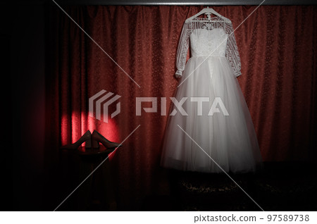 The wedding dress hangs on the cornice, a beam of colored light is directed at the dress. 97589738