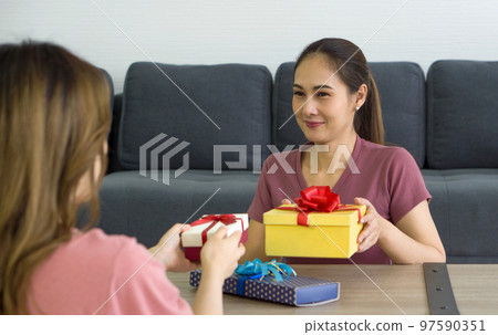 Two Asian women enjoy giving each other gift boxes on a special occasion. Two Asian women enjoy giving each other gift boxes on a special occasion. 97590351