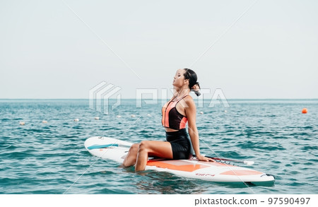 Sea woman sup. Silhouette of happy young woman in pink bikini, surfing on SUP board, confident paddling through water surface. Idyllic sunset. Active lifestyle at sea or river. 97590497