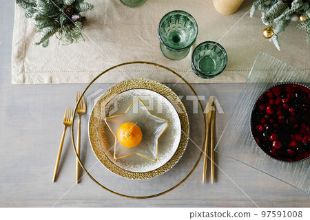 Stylish Christmas dinner setting. Gold and white plates, a star-shaped plate with tangerine. Berry pie on the table Stylish Christmas dinner setting. Gold and white plates, a star-shaped plate with tangerine. Berry pie on the table 97591008