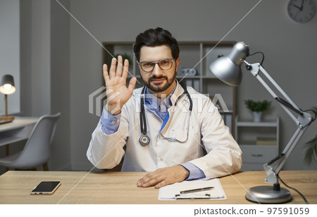 Doctor sitting at desk, looking at camera, waving hand, greeting patient at online consultation Doctor sitting at desk, looking at camera, waving hand, greeting patient at online consultation 97591059