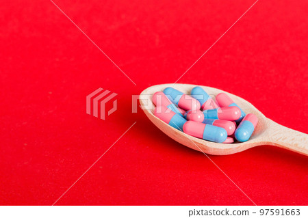 Vitamin capsules in a spoon on a colored background. Pills served as a healthy meal. Red soft gel vitamin supplement capsules on spoon 97591663