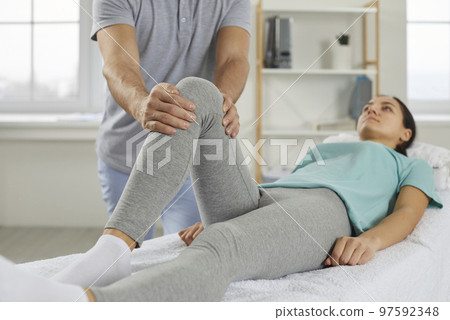 Physiotherapist examining and helping young woman who has knee pain after injury 97592348