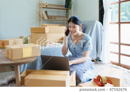 Starting small business entrepreneur of independent Asian female online seller talking on the phone with a customer and packing products for delivery to the customer. and SME delivery concept. 97592676