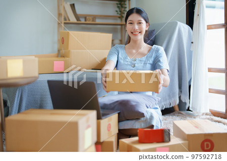 Starting small business entrepreneur of independent Asian woman smiling using computer laptop with cheerful success of online marketing package box items and SME delivery concept. 97592718
