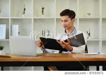Concentrated asian man investor analyzing financial data and using laptop at his office desk 97593071