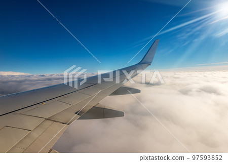 Commercial Airplane Flying over the Clouds - Looking through the Plane Window 97593852