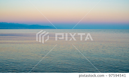 The surface of the water in the Issyk Kul mountain lake in Kyrgyzstan at sunset.Pastel and soft tones of water and sky against the background of mountains. 97594541