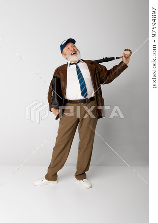 Portrait of senior old man in leather jacket posing with briefcase and umbrella over grey background. Cheerfully laughing 97594897