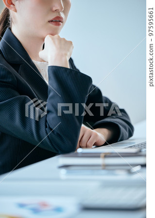 A young woman thinking with her chin resting on her desk 97595661