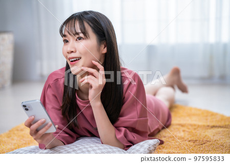 Young woman lying on carpet and using smartphone Young woman lying on carpet and using smartphone 97595833