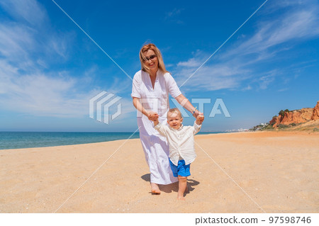 Young caucasian mother walks with her happy son along the sea beach in the summer near the sea. Concept of happy childhood and motherhood. 97598746
