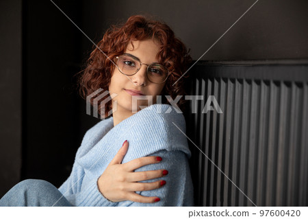 A girl with curly hair sits by the heater and warms herself. A girl with curly hair sits by the heater and warms herself. 97600420