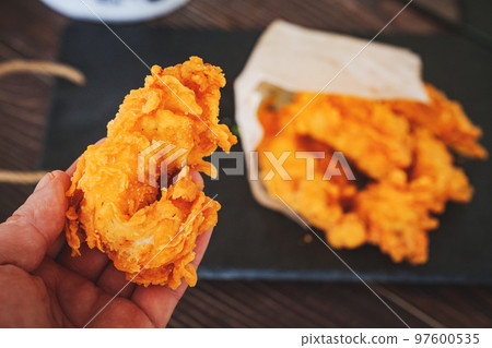 arm and meat strips on a black tray. strips of meat fried in breading.  97600535