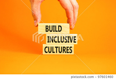 Build inclusive cultures symbol. Concept words Build inclusive cultures on wooden blocks. Businessman hand. Beautiful orange background. Business build inclusive cultures concept. Copy space. 97601460