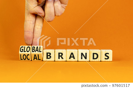 Global or local brands symbol. Concept words Global brands and Local brands on wooden cubes. Businessman hand. Beautiful orange background. Business global or local brand concept. Copy space. Global or local brands symbol. Concept words Global brands and Local brands on wooden cubes. Businessman hand. Beautiful orange background. Business global or local brand concept. Copy space. 97601517