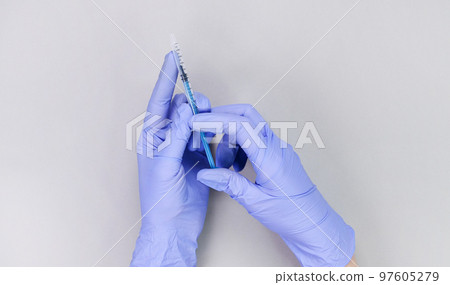 Hands in blue gloves of doctor or nurse holding syringe with liquid vaccine over grey background with copy space. New vaccine. Unknown vaccine. Medical gloves. Hands in blue gloves of doctor or nurse holding syringe with liquid vaccine over grey background with copy space. New vaccine. Unknown vaccine. Medical gloves. 97605279
