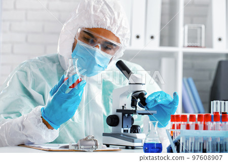 Medical worker in protective gown looking in microscope Medical worker in protective gown looking in microscope 97608907
