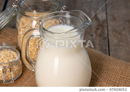 Glass pitcher of milk and oat flakes on wooden table Glass pitcher of milk and oat flakes on wooden table 97609052