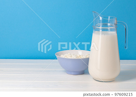 Glass pitcher of milk and bowl of cottage cheese on wooden table 97609215