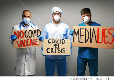 People in medical gowns wearing face masks protesting and holding placards 97609318