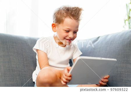 Little boy sitting on sofa and using digital tablet at home 97609322