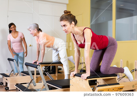 Female instructor helps women perform an exercise on a combined chair Female instructor helps women perform an exercise on a combined chair 97609363