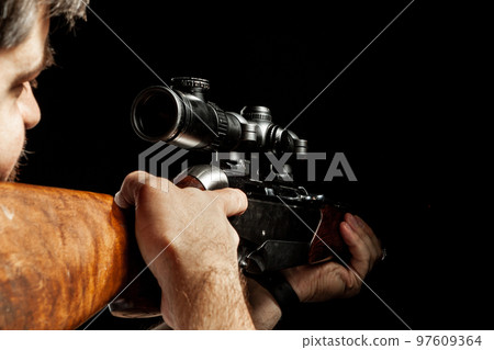 Unrecognizable man aiming with a hunting rifle in dark Unrecognizable man aiming with a hunting rifle in dark 97609364