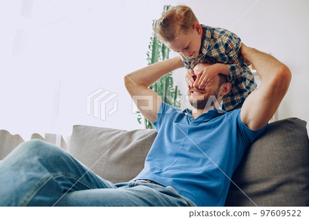 Little boy covers father's eyes with his hands in living room Little boy covers father's eyes with his hands in living room 97609522