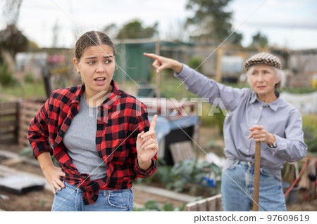Two angry casual women neighbors of different ages arguing during the vegetable garden season on sunny day of spring Two angry casual women neighbors of different ages arguing during the vegetable garden season on sunny day of spring 97609619
