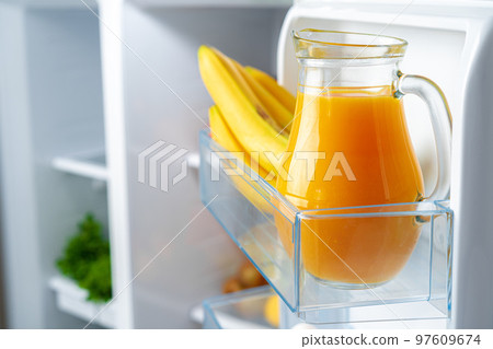 Glass pitcher of orange juice and fruits on fridge shelf 97609674