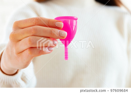 Woman in white sweater holding pink menstrual cup in hands close up 97609684