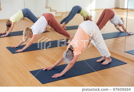 Three women standing in downward-facing dog pose in studio 97609884