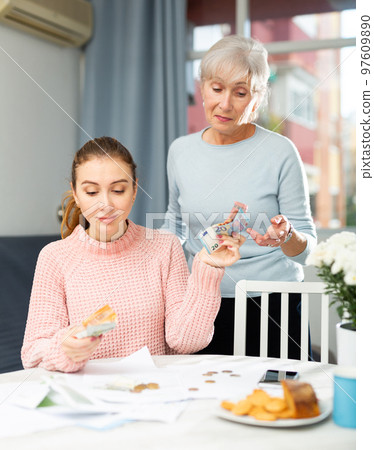 Young woman holding out banknotes to aged mother at home table 97609890