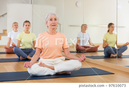 People of different ages sitting in lotus position practicing meditation in yoga class People of different ages sitting in lotus position practicing meditation in yoga class 97610073
