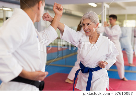 Man and senior woman sparring during group karate training 97610097