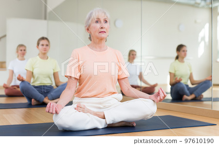 Senior woman sitting on mat in lotus pose during yoga training Senior woman sitting on mat in lotus pose during yoga training 97610190