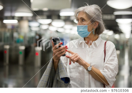 Caucasian woman in mask with smartphone in subway station 97610306