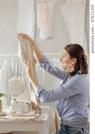 woman seamstress in workshop sews clothes for sale. cozy workplace, small business or hobby 97611205