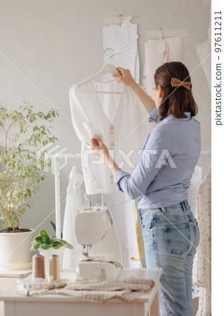 woman seamstress in workshop sews clothes for sale designs patterns. cozy workplace, small business 97611211
