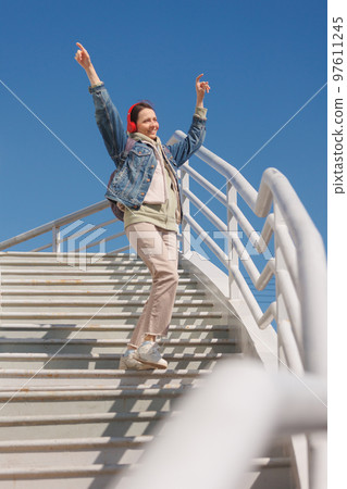 woman dances and sings on stairs, listens to music or podcast with red headphones, full-length woman dances and sings on stairs, listens to music or podcast with red headphones, full-length 97611245