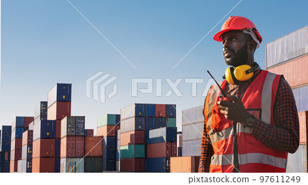 American African engineer or factory worker man using walkie talkie and check up goods at container cargo harbor. American African engineer or factory worker man using walkie talkie and check up goods at container cargo harbor. 97611249