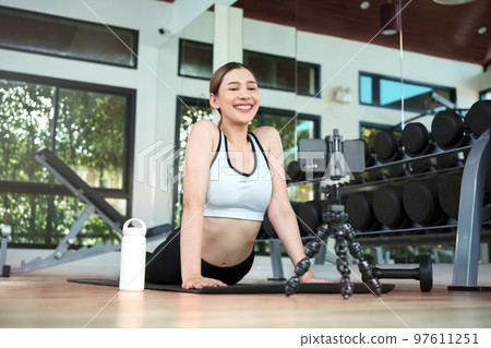 Young woman watching fitness video or having video conference with fitness trainer at smartphone screen. 97611251